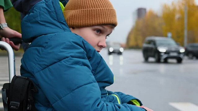 a 10-year-old disabled child in a wheelchair on the street with his mother for a walk. in autumn. High quality FullHD footage