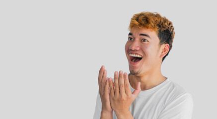 Young Asian man in white t-shirt having a big surprise, isolated on gray background. The concept of...