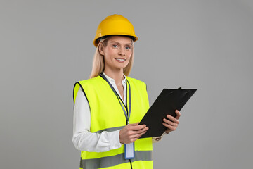 Engineer in hard hat holding clipboard on grey background