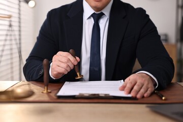 Notary stamping document at wooden table in office, closeup