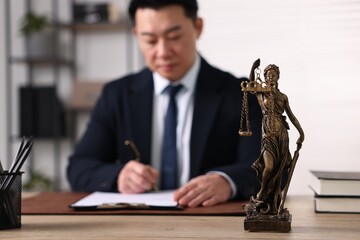 Notary working at wooden table in office, focus on statue of Lady Justice