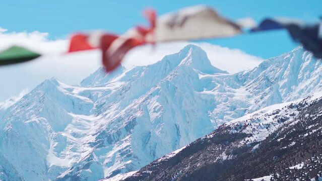 Defocused Buddhist Prayer flags waving in the wind in front of snow covered Himalayan mountains during the winter season at Keylong in Himachal Pradesh, India. Selective focus on the mountains.