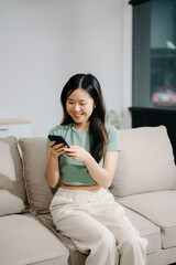 Asian woman using the smartphone and tablet on the sofa at home
