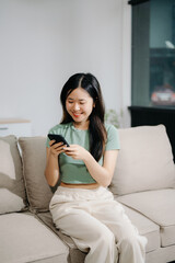 Obraz premium Asian woman using the smartphone and tablet on the sofa at home