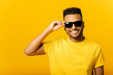 Handsome attractive young Indian guy in sunglasses posing isolated on yellow background. Carefree...