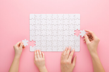 Mother and daughter hands playing and assembling white puzzle pieces on pink table background. Pastel color. Family activities. Spending time together. Closeup. Point of view shot. Top down view. - obrazy, fototapety, plakaty