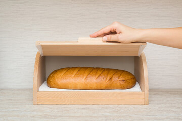 Young adult woman hand opening or closing wooden breadbox with white bread inside on table top at home kitchen. Closeup. Front view.