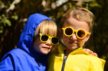 Children in bright raincoats and sunglasses on a sunny day. Summer rain, changeable weather in...