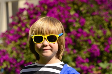 Portrait of a cute boy with long hair wearing sunglasses. Concept: happy childhood, advertising for a kindergarten.