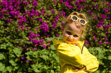 Portrait of a cute 5 year old girl, The child laughs. Blonde girl in a yellow raincoat in the bright sun and sunglasses.