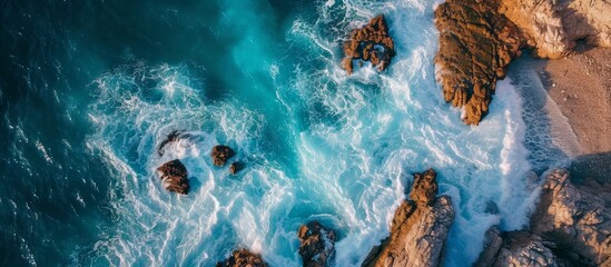 An electric blue pattern of water, liquid, and geological phenomenon as waves crash against rocks on the beach. - obrazy, fototapety, plakaty
