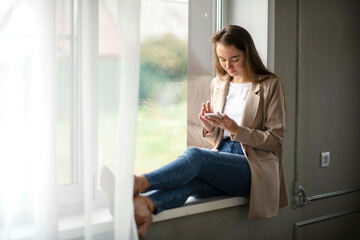 Fototapeta premium Work-life-balance, caucasian Female Manager on the windowsill in the hall with smartphone