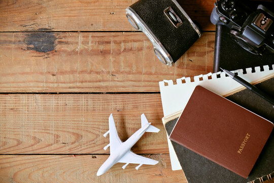 Travel concept with passport, camera, notebook and airplane on wooden background