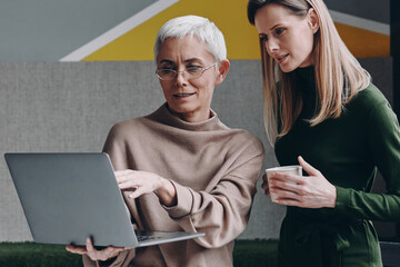Two confident women using technologies and communicating while working in office together
