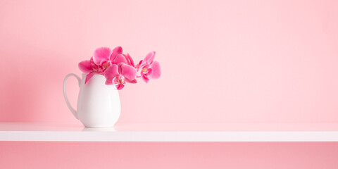 Pink orchid on white shelf and on background of pink wall. Greeting card for Mother's Day, Easter, Happy Woman's Day, Wedding, Birthday, Valentine's Day