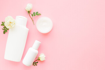 Fototapeta na wymiar Different white plastic toiletries and rose flowers on light pink table background. Pastel color. Care about clean and soft body skin. Women daily beauty products. Empty place for text. Top down view.