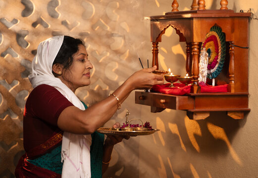 Indian woman lighting diya in front of god during morning puja rituals at home - concept of mindfulness, religious faith and sacred faith