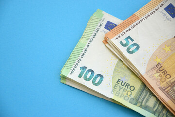 Many banknotes of 100 and 50 Euro bills on light blue paper background
