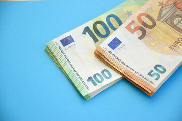 Many banknotes of 100 and 50 Euro bills on light blue paper background