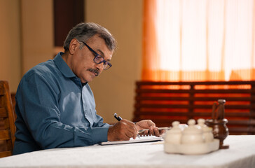 Fototapeta na wymiar Indian senior man calculating monthly expenses or budget at at home - concept of financial planning, discipline and household expenses