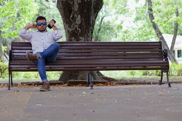 latin man with cell phone sitting on park bench