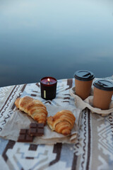 aesthetic photo. picnic on the pier with coffee and croissants, chocolate and candles