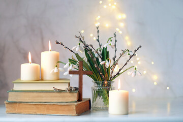 christian cross, religion books, candles and bouquet with Snowdrop flowers on table, abstract light...