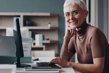 Senior businesswoman looking at camera and smiling while sitting at her working place in office