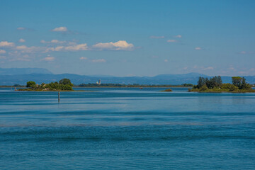 A channel marker shows the edge of a navigable channel in the Grado section of the Marano and Grado Lagoon in Friuli-Venezia Giulia, NE Italy. Santuario di Barbana Church background. August