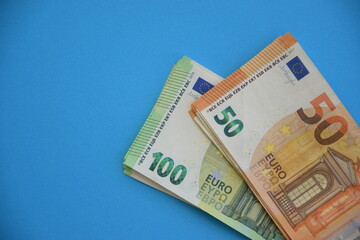 Many banknotes of 100 and 50 Euro bills on light blue paper background