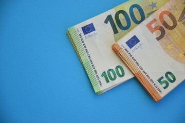 Many banknotes of 100 and 50 Euro bills on light blue paper background
