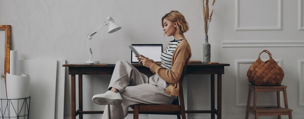 Confident young woman using digital tablet while sitting at her creative working place