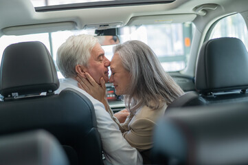 Mature Caucasian couple sitting in a new car and rejoicing at the purchase. 