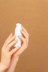 Female palms holding white bottle jar with face moisturizing cream dispenser on isolated peach background. Ready template for brand presentation. Skin care ad, copy space. Vertical photo