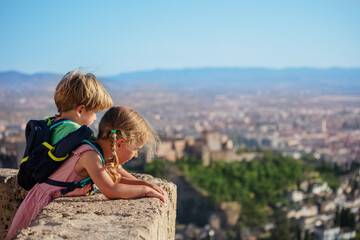 Fototapeta na wymiar Blond siblings stand on viewpoint admire Alhambra castle