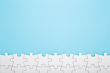 Row of completed different white puzzle pieces on light blue table background. Pastel color. Closeup. Empty place for text. Top down view. - obrazy, fototapety, plakaty