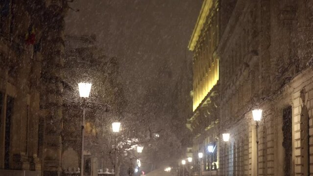 Winter in Bucharest. 4K video during a night snowfall on the streets of the city view to the old town, tilt camera movement. Travel to Romania.