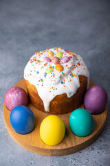Easter kulich with candied fruits in white glaze with colorful sprinkles and painted eggs. Traditional Easter pastry. Easter holiday. Close-up, selective focus.