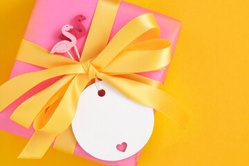 Banner with pink gift box with flamingo figurines and yellow bow on yellow background. Place for your text