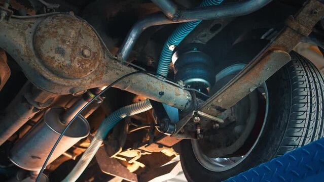 Intricate view of a car's undercarriage with suspension springs and exhaust system, during a mechanical check-up on a lift.