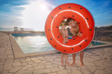 Kids hold watermelon float at poolside look out from the hole