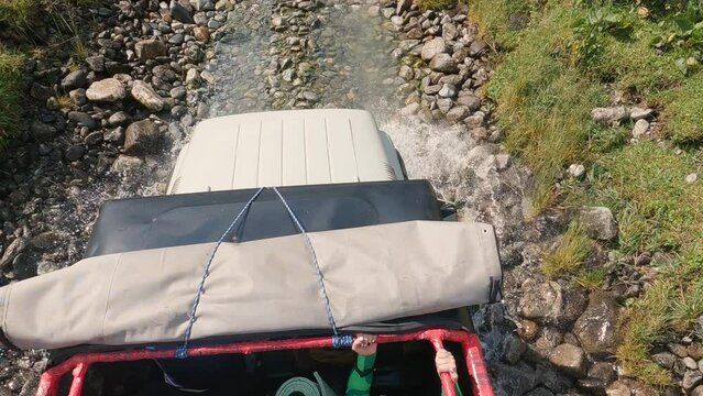 SUV driving along a river and rocks in the mountains. Top view of the bonnet, people in the cabin and the road. Off-road driving on a mountain road. Slow motion