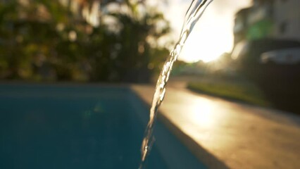 Close up stream of water flowing from a green hose and filling a clean blue swimming pool in the backyard. Weekly pool maintenance and cleaning - Powered by Adobe