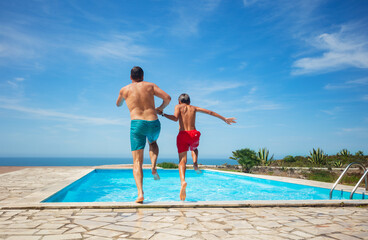Joyful dynamic pool jump of father and son by the sea view