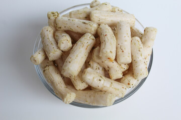 Fish crackers in small cylinder shape. Snack from Indonesia, called krupuk ikan tongkol. In a transparent glass bowl, isolated on white background