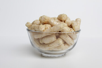 Fish crackers in small cylinder shape. Snack from Indonesia, called krupuk ikan tongkol. In a transparent glass bowl, isolated on white background