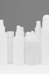 Facial skin care products on white table, assortment of cosmetic bottles on peach background, copy space. Vertical photo. Beauty ad. A clean ready-made template for brand presentation