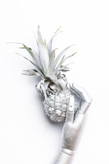 Artistic futuristic image with robotic silver hand holding metallic pineaplle on white background, vertical image.
