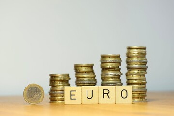 Steigender Eurokurs symbolisiert durch eine Euro Geldmünze, Stapel aus Münzgeld und den Schriftzug Euro, die Währung Euro gewinnt an Wert durch finanziellen Aufschwung, steigendes Gehalt und mehr Geld - obrazy, fototapety, plakaty