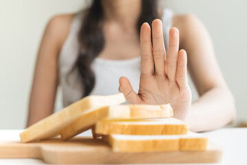 Gluten allergy, asian young woman hand push out, refusing to eat white bread slice on chopping board in food meal at home, girl having a stomach ache. Gluten intolerant and Gluten free diet concept. - obrazy, fototapety, plakaty